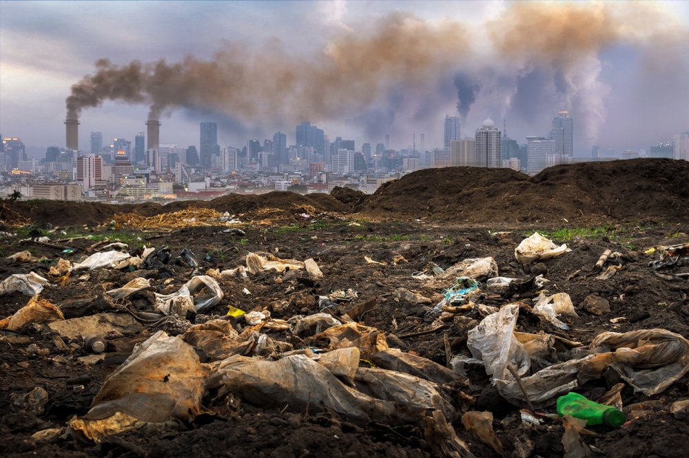 Plastic waste on land with thick, black clouds are coming from a factory nearby