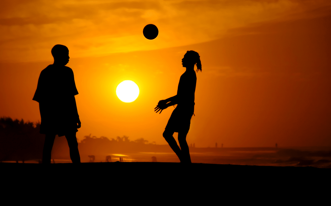 Silhouette of two people playing football at the sunset on the beach.