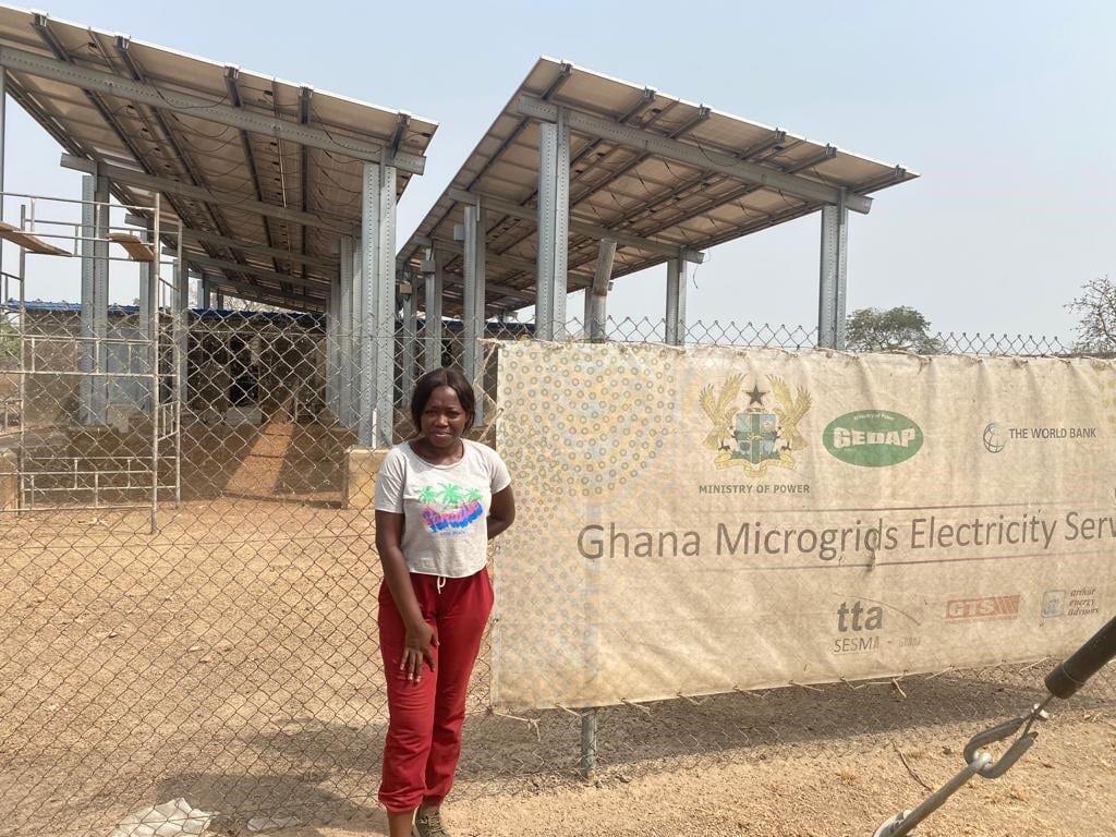 Tracy stands in front of a solar mini-grid implemented in one island community in Ghana