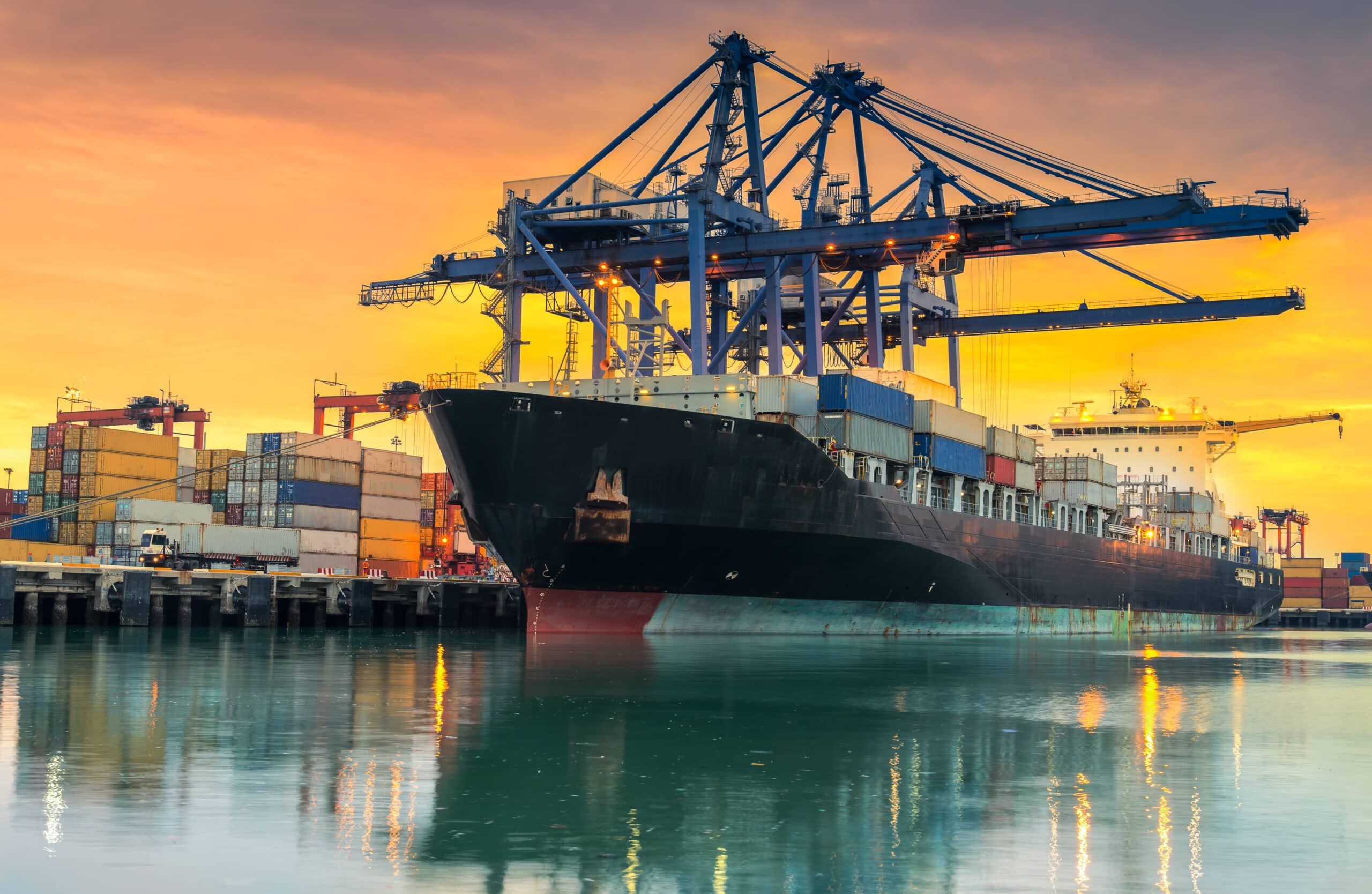 Cargo ship loading containers at sunset.